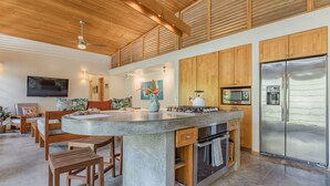 A modern kitchen with a large island, wooden cabinets, stainless steel appliances, and a flat-screen TV. - Tropical Modern Home w/pool near the beach & surf (Nosara)