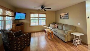 A living room with a sofa, a television, a ceiling fan, and a window with blinds. - 3- Bedroom cottage near Pleasant Lake in Cadillac (Cadillac)