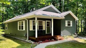 A single-story house with a front porch, a small deck, and a well-maintained lawn. - 3- Bedroom cottage near Pleasant Lake in Cadillac (Cadillac)