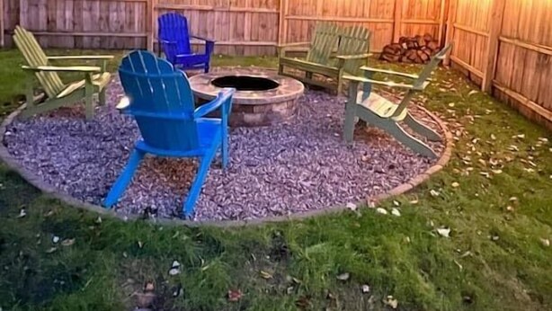 A backyard with a fire pit, Adirondack chairs, and a wooden fence with string lights. - 3 - Bedroom Cottage Near Lake Mitchell in Cadillac (Cadillac)