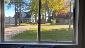 A window with a view of a residential street, houses, and trees. - 3 - Bedroom Cottage Near Lake Mitchell in Cadillac (Cadillac)