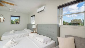 A hotel room with two beds, a grey sofa, and a window with a view of greenery.