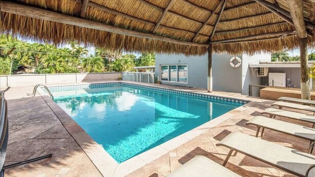 A swimming pool with a thatched roof, lounge chairs, and a view of palm trees.