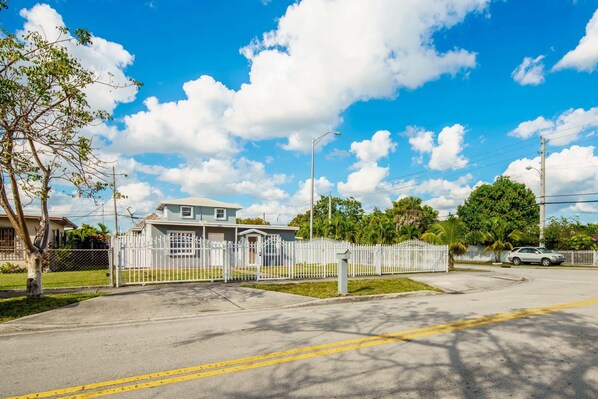 A residential street with a house, white fence, and clear sky.
