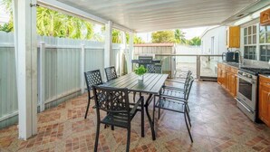 A covered patio with a dining table and chairs, a grill, and a kitchen area with cabinets and appliances.