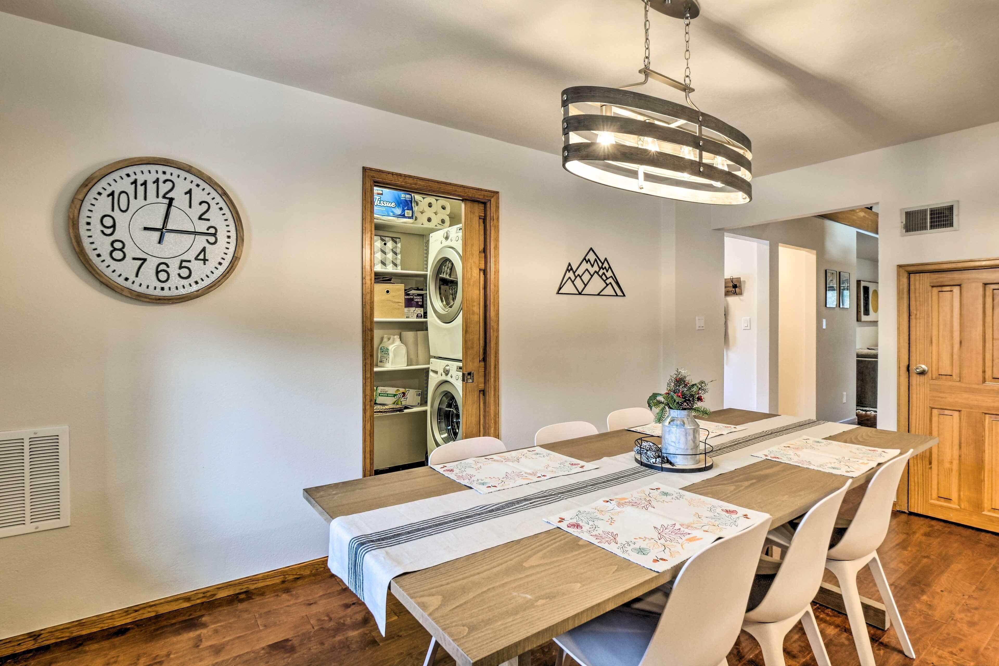A dining area with a wooden table, white chairs, a wall clock, and a pendant light.