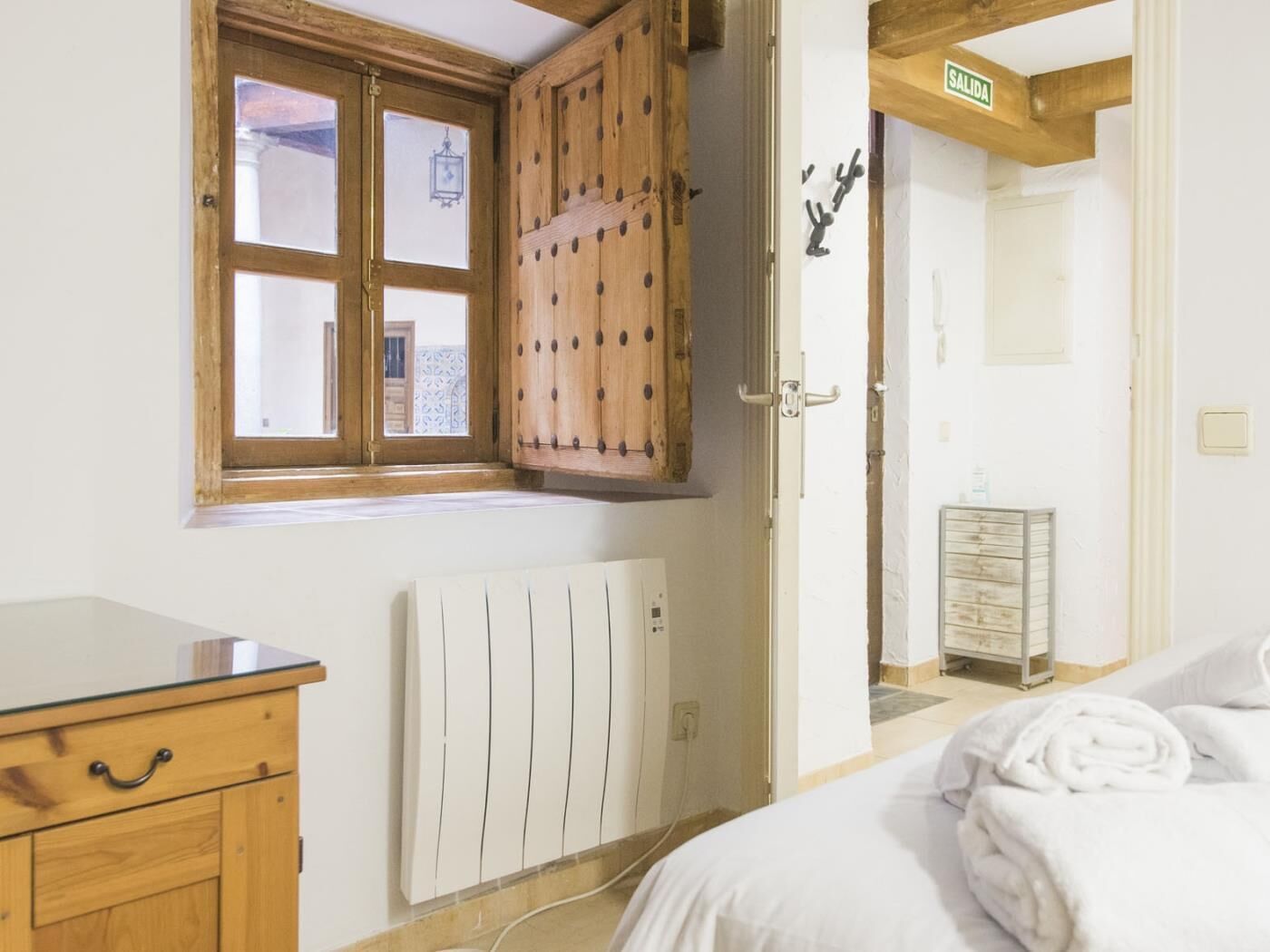 Una camera da letto con un armadio in legno, un termosifone, un letto con biancheria bianca e una finestra con persiane in legno.