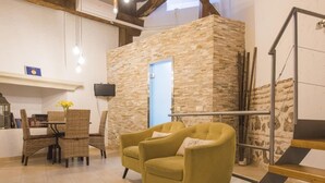 Ein modernes Wohnzimmer mit einer Wand aus Stein, einem gelben Sessel, Korbmöbeln und einer Treppe.