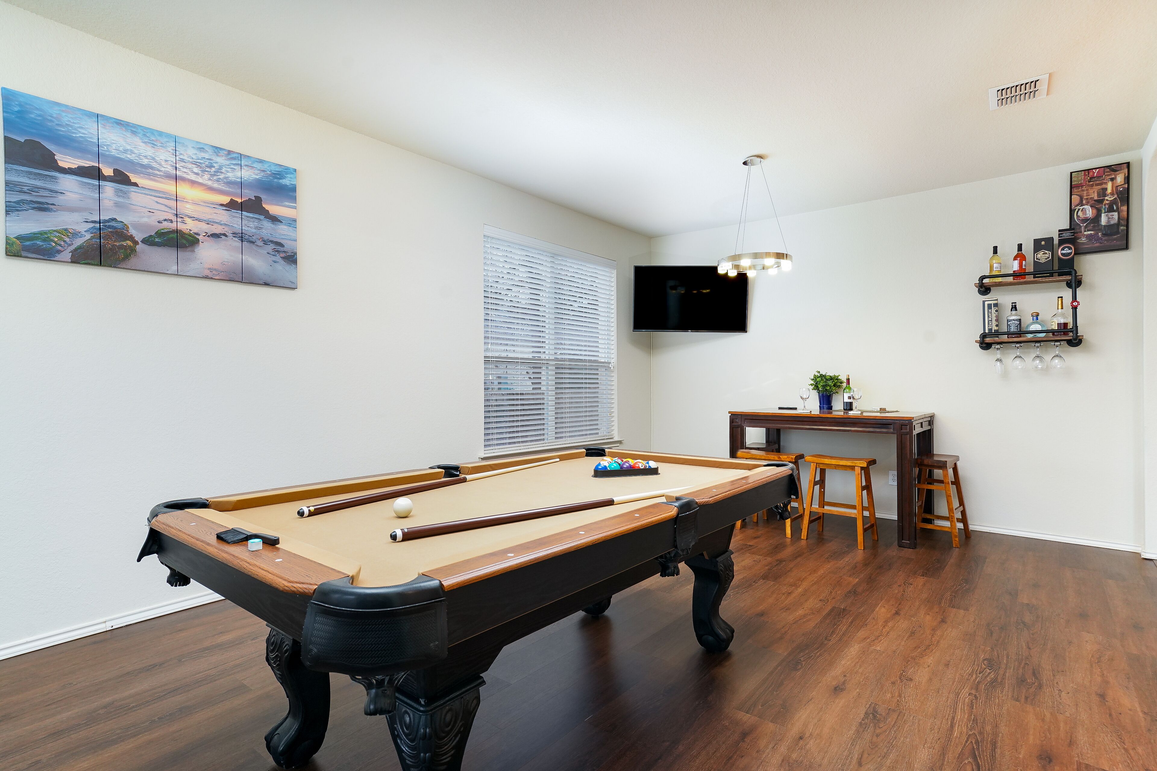 Une table de billard dans une pièce dotée d’un plancher en bois, d’un téléviseur fixé au mur et d’une fenêtre avec des stores.