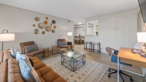 Una sala de estar moderna con un sofá marrón, una mesa de centro de vidrio y un comedor con una mesa y sillas de madera.