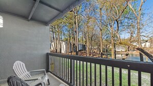 Un espacio al aire libre techado con dos sillas Adirondack, una mesita y una barandilla con vistas al agua y árboles.