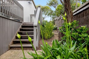 A residential property with a wooden staircase leading to a grey door, surrounded by lush greenery and a tree.