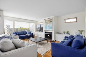 A modern living room with a fireplace, blue sofas, and a large window.