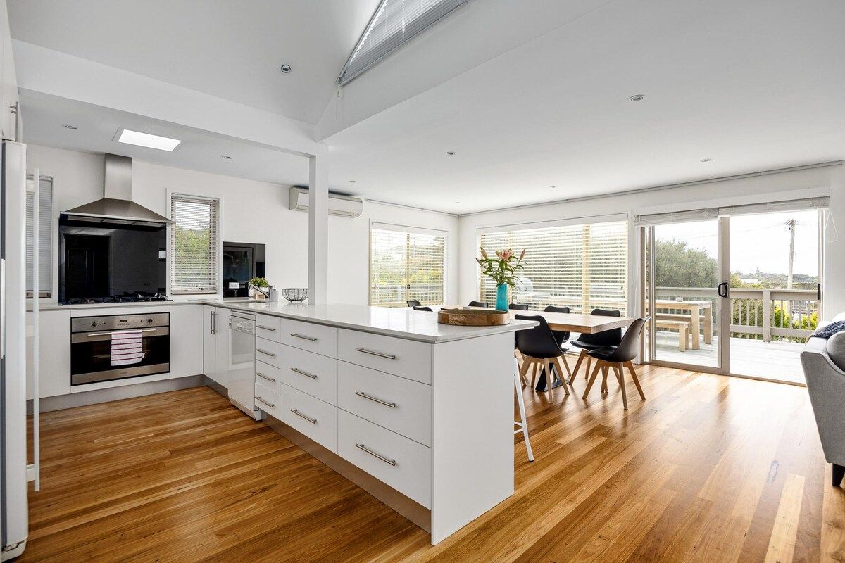 A modern kitchen with white cabinetry, a central island, and a dining area with a view.