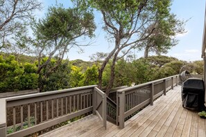 A wooden deck with a railing, surrounded by trees and shrubs.