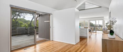 A spacious room with a wooden floor, a sliding glass door leading to an outdoor deck, and a view of the outdoors.