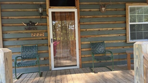 A wooden cabin with a sliding glass door, two green metal chairs, and a welcome sign with a number. - Beautiful Cabin in quiet rural location (Sylvania)