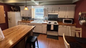 A kitchen with white cabinets, a wooden countertop, a stove, a microwave, and a window. - Beautiful Cabin in quiet rural location (Sylvania)