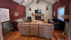 A cozy living room with a stone fireplace, a ceiling fan, and mounted deer heads. - Beautiful Cabin in quiet rural location (Sylvania)