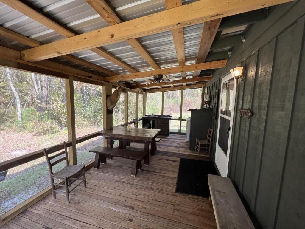 An outdoor covered patio with wooden benches and tables, a grill, and a view of the surrounding forest.