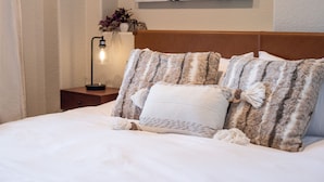 Un lit bien fait, avec des oreillers à rayures et blancs, une lampe de chevet et un tableau accroché au mur.