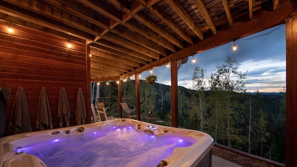 Un bain à remous doté d’un plafond en bois et offrant une vue sur une chaîne de montagnes boisées.