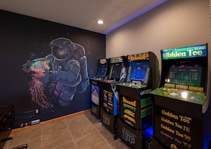 A row of vintage arcade machines, including 'Rampage' and 'Golden Tee', in a room with a mural of an astronaut. - Panoramic Views from a Large Peaktop Retreat with Hot Tub, Sauna, & Axe-Throwing (Conifer)