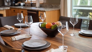 Une table à manger dressée avec des assiettes, des verres et un saladier de fruits.