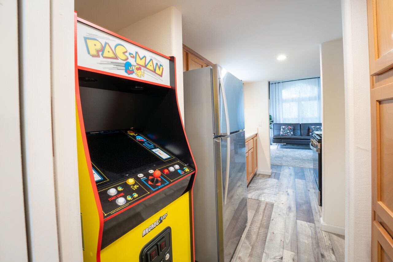 A Pac-Man arcade machine in a hallway with a kitchen area visible in the background.