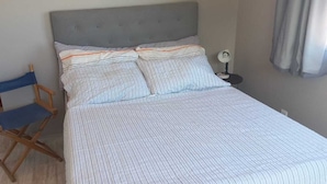 A bedroom with a bed, a nightstand, a lamp, and a blue folding chair. - Suite with beautiful sea view!! (Florianópolis)