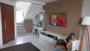 A modern living room with a television, a sofa, a coffee table, and a staircase leading to another level. - Suite with beautiful sea view!! (Florianópolis)