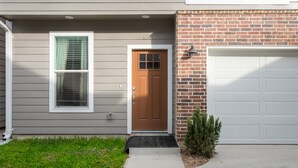 Une maison d’habitation avec une porte d’entrée marron, une porte de garage et un petit arbre dans le jardin.