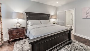 Une chambre à coucher avec un lit en bois foncé, deux tables de chevet avec des lampes, un ventilateur de plafond et une porte donnant sur une salle de bain.