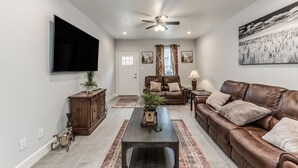 Un salon avec un canapé en cuir marron, une table basse, un téléviseur à écran plat et un ventilateur de plafond.