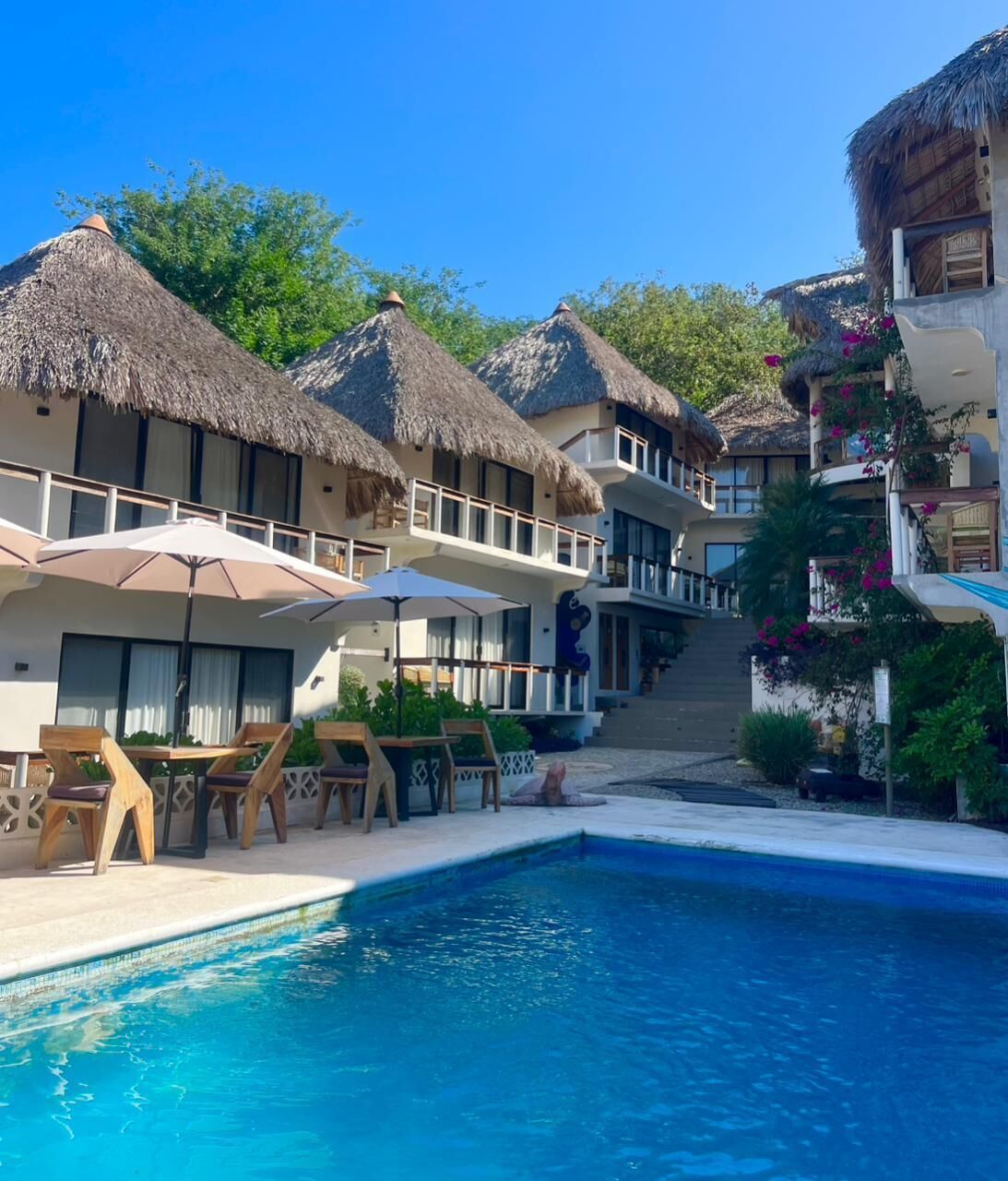 A resort with a pool, thatched-roof buildings, and outdoor seating.