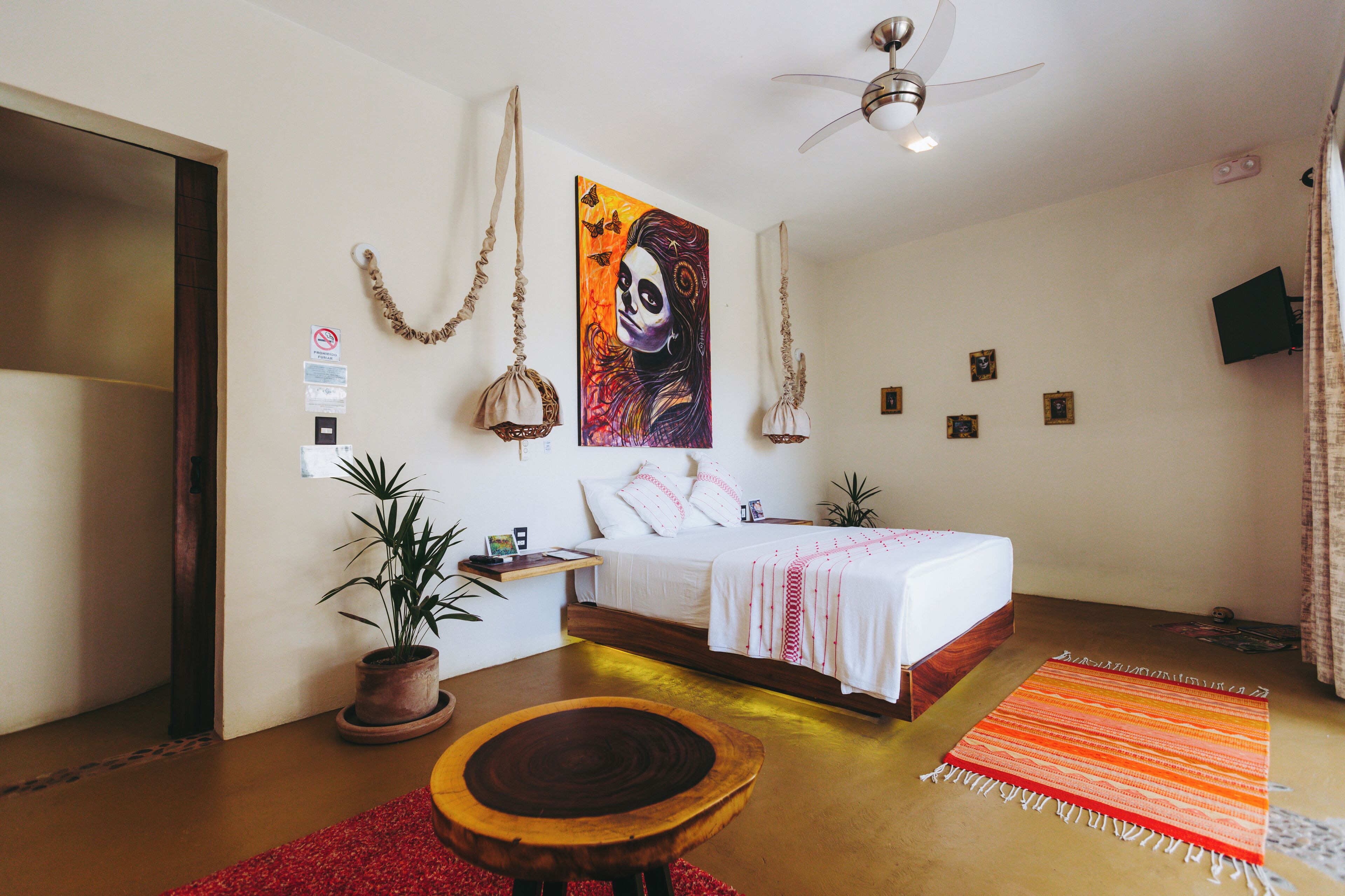 A bedroom with a bed, a ceiling fan, a TV, and a red rug.