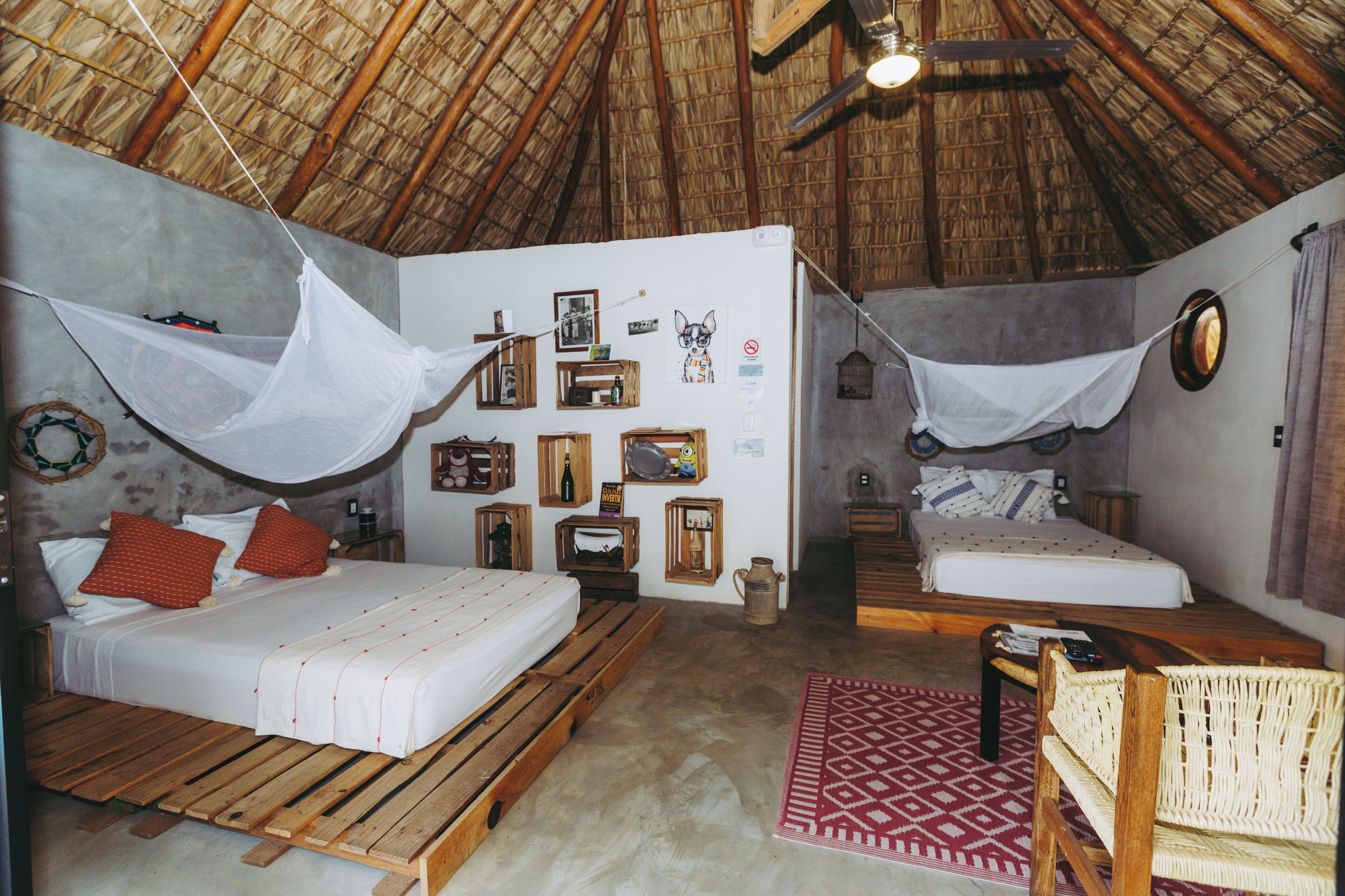 Une chambre avec deux lits, un plancher en bois, un toit de chaume et un mur décoré de divers objets.