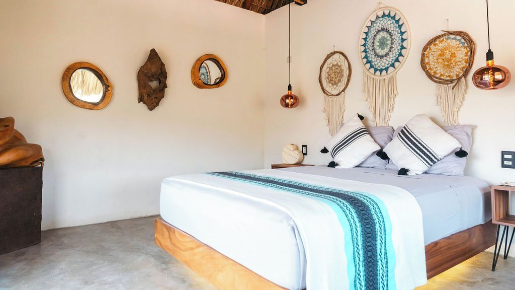 A bedroom with a bed, a wooden headboard, a nightstand, and wall decor including mirrors and dreamcatchers.