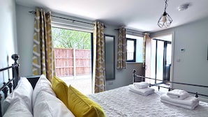 Ein Schlafzimmer mit Bett, Kissen, einem Fenster, Vorhängen, einem Spiegel und einer Pendelleuchte.
