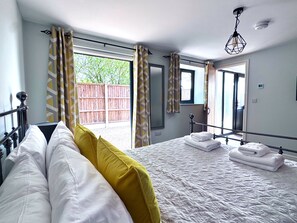 A bedroom with a bed, pillows, a window, curtains, a mirror, and a hanging light fixture.