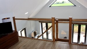Ein Zimmer mit schrägem Dach, einer Holztreppe, einem Fernsehschrank und einem großen Fenster.