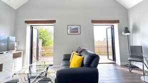Ein geräumiges Wohnzimmer mit hohen Decken, einem schwarzen Ledersofa, einem Glastisch, einem Fernseher und einem gerahmten Bild an der Wand.