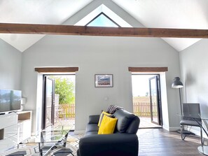 A spacious living room with a high ceiling, a black leather sofa, a glass coffee table, a TV, and a framed picture on the wall. - Pet friendly getaway - private hot tub, enclosed garden - countryside views (Dilham)