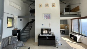 A modern living space with a staircase, a flat-screen TV, a dining area, and a large window offering a view. - Villa Achilles (Pera Melana)