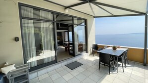 A balcony with a table and chairs, a sliding glass door, and a view of the sea. - Villa Achilles (Pera Melana)