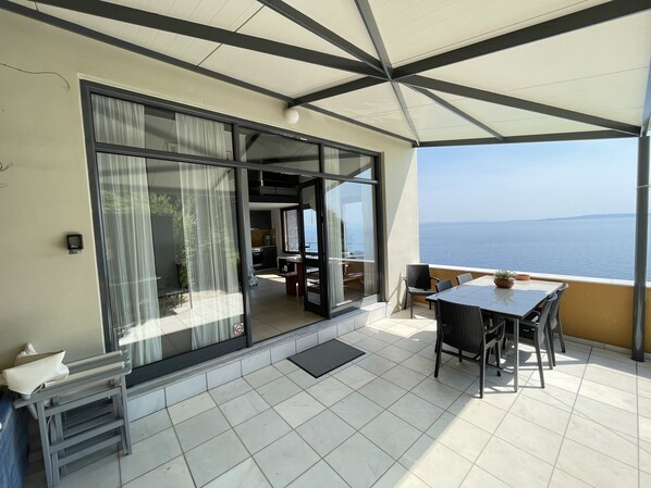 A balcony with a table and chairs, a sliding glass door, and a view of the sea.