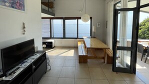 A modern kitchen with a large window overlooking the sea, a wooden dining table, and a TV on a cabinet. - Villa Achilles (Pera Melana)