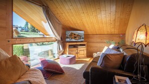 A cozy living room with a wooden ceiling, a leather sofa, a coffee table, and a television on a wooden cabinet. - Chalet Antigone - ski holiday for 8 with mountain view - OVO Network (Saint-Jean-de-Sixt)