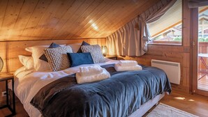 A cozy wooden cabin bedroom with a bed, pillows, and a window with curtains. - Chalet Antigone - ski holiday for 8 with mountain view - OVO Network (Saint-Jean-de-Sixt)