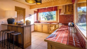 A kitchen with wooden cabinets, a tiled backsplash, a window with a view of greenery, and a bar area with stools. - Chalet Antigone - ski holiday for 8 with mountain view - OVO Network (Saint-Jean-de-Sixt)